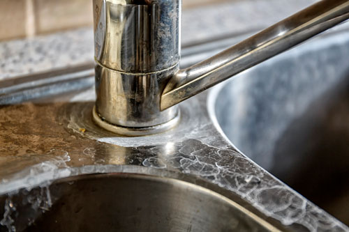 Close-up of a kitchen tap and sink with hard water calcification.