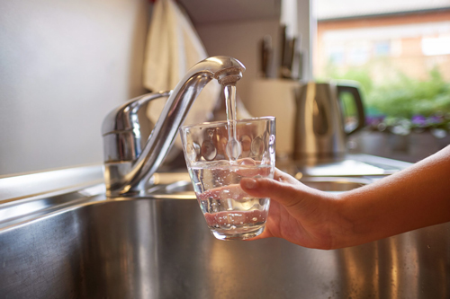 hand holding a glass of water being filled up at a kitchen sink