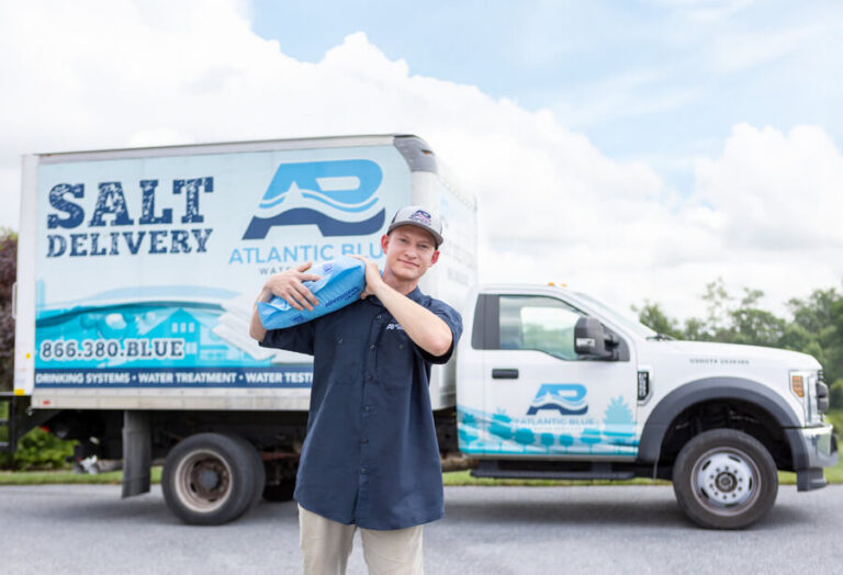 Atlantic Blue technician carrying a bag of water softener salt in front of a parked delivery truck