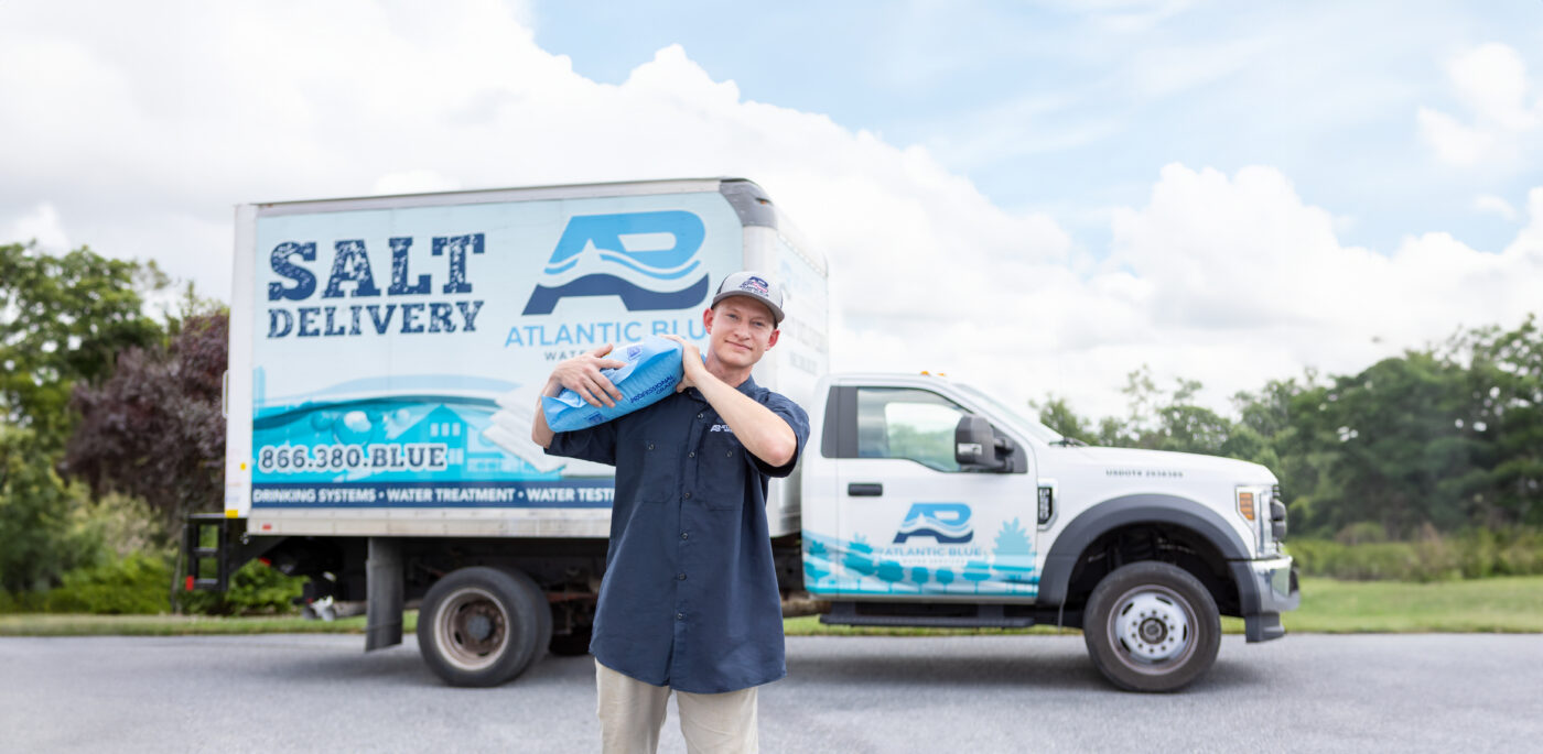Atlantic Blue technician carrying a bag of water softener salt in front of a parked delivery truck